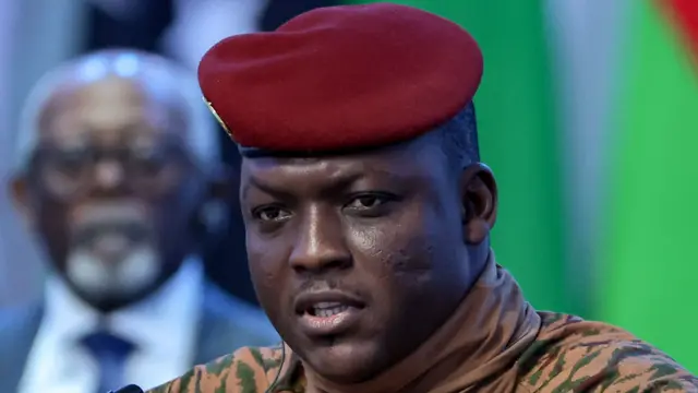 Portrait d'Ibrahim Traoré en tenue militaire beige et béret rouge.