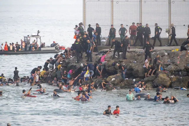 Foule de migrants traversant la frontière vers Ceuta, illustrant l’ampleur de la crise humanitaire.