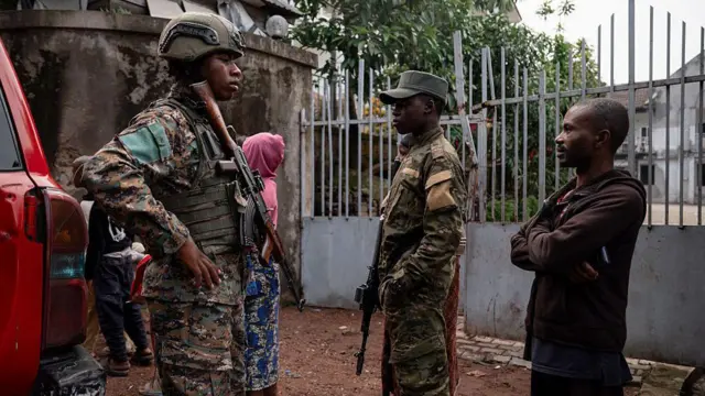 Deux militaires en uniforme aux côtés d’un civil et d’une femme en arrière-plan